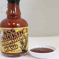 Ass Kickin' Moonshine Pepper Mash on a table beside a small bowl of sauce.